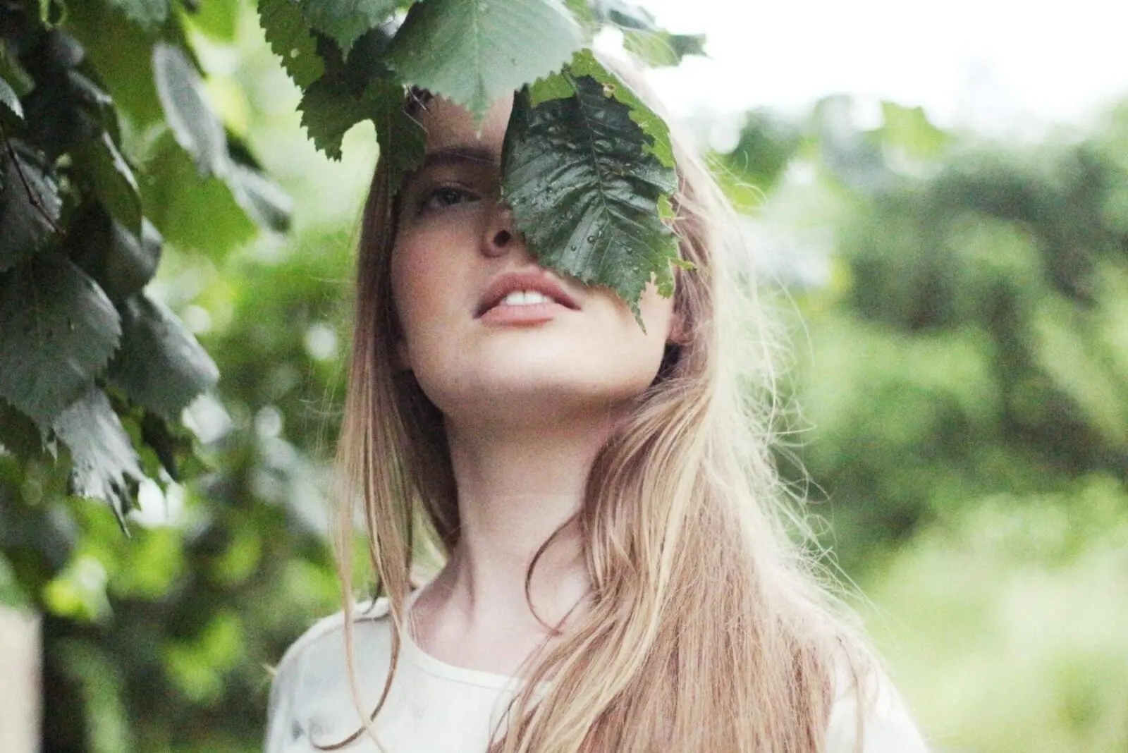 A woman with long hair is hiding behind a tree, possibly planning her wedding.