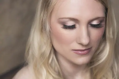 A blond woman with long eyelashes is posing for a photo at a wedding.