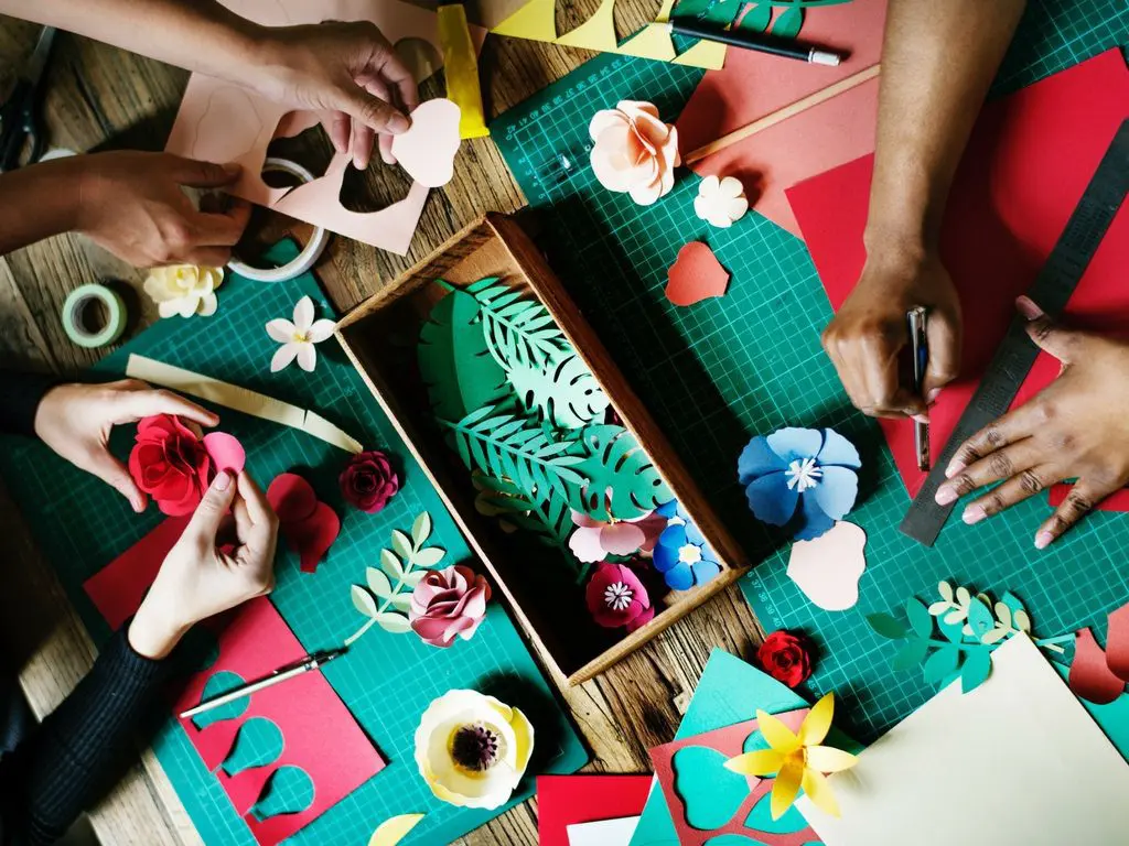 A group of people engaged in wedding planning and creating intricate paper crafts on a table.