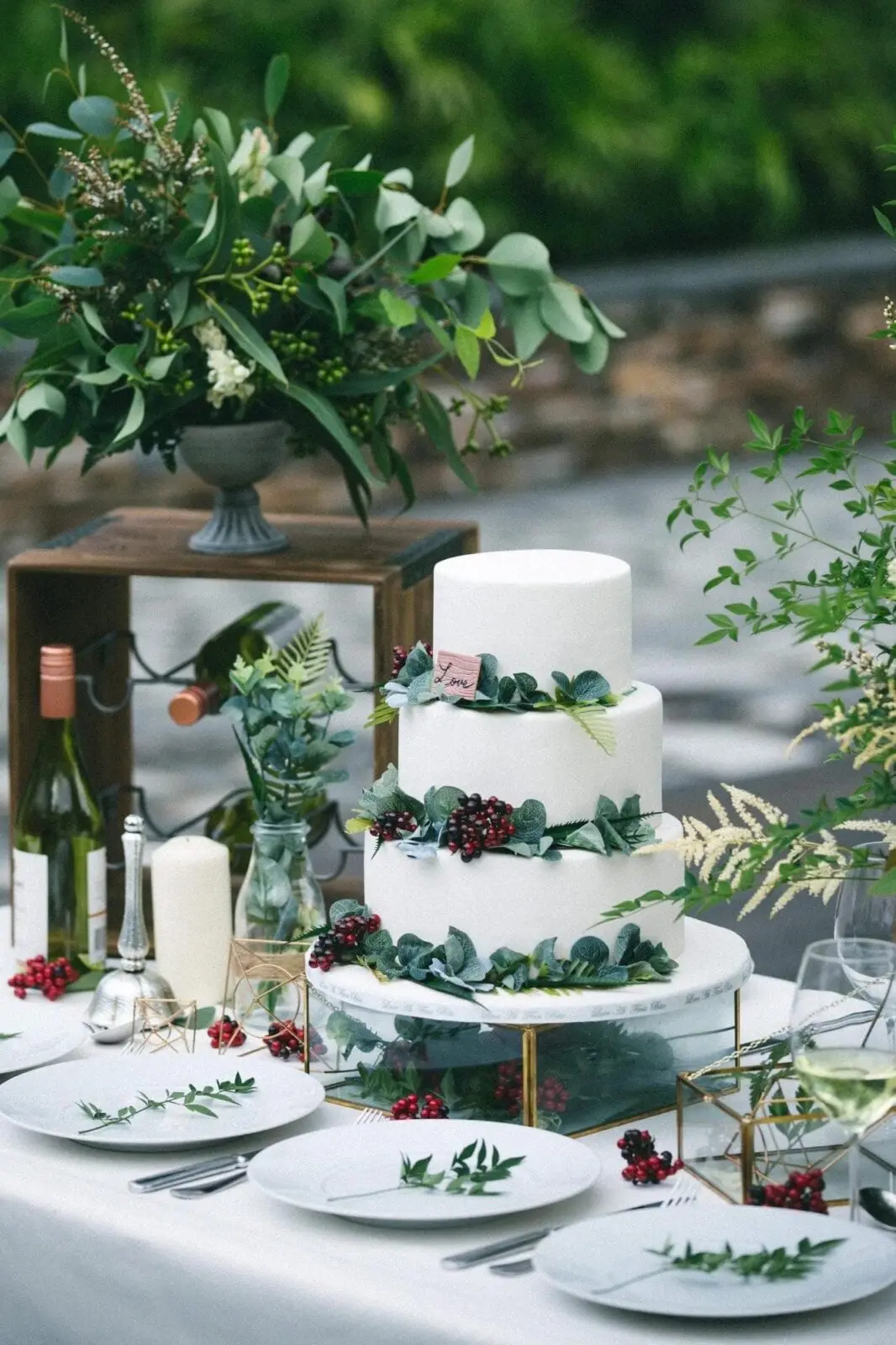 A white wedding cake with greenery and berries on a table in the UK.