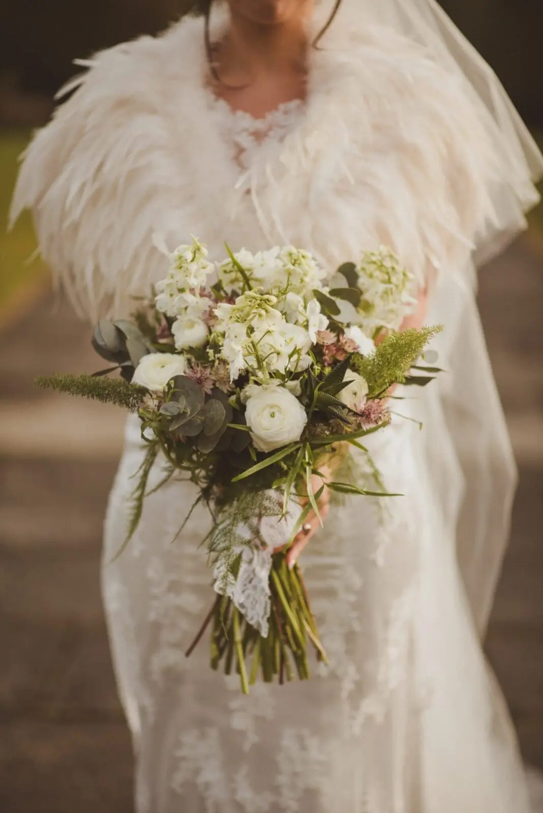 A bride holding a bouquet of white flowers and feathers for her wedding.