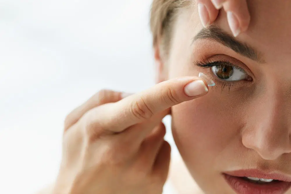 A woman is putting wedding contact lenses on her eye.