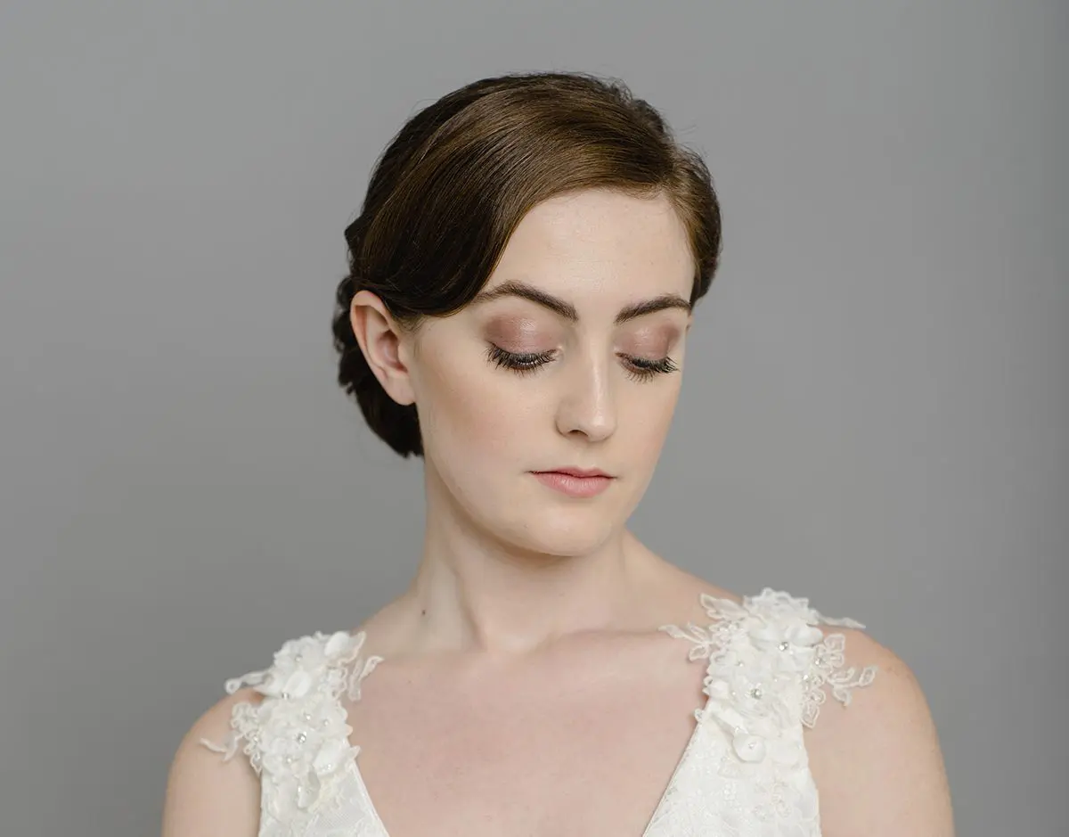 A woman in a white wedding dress is posing on a gray background for her wedding.