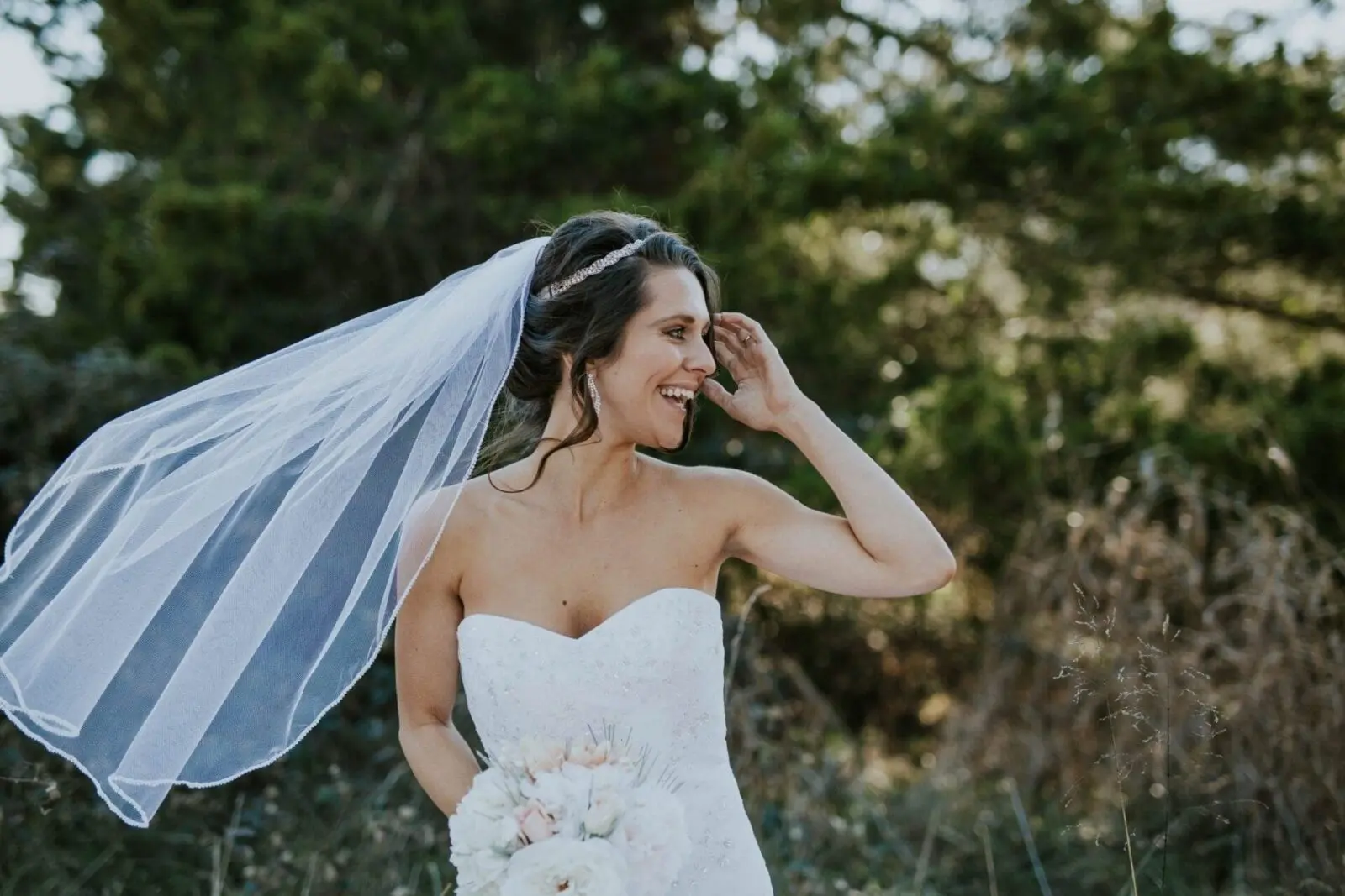 Bride in a white dress and flowing veil smiles showing perfect white teeth.