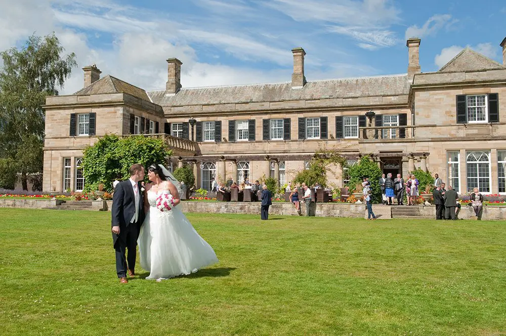 A bride and groom standing in front of a large mansion, highlighting their special day in the wedding business.