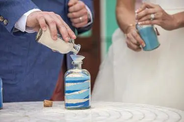A bride and groom participate in a sand ceremony during their wedding, symbolizing the blending of their lives and families into one.
