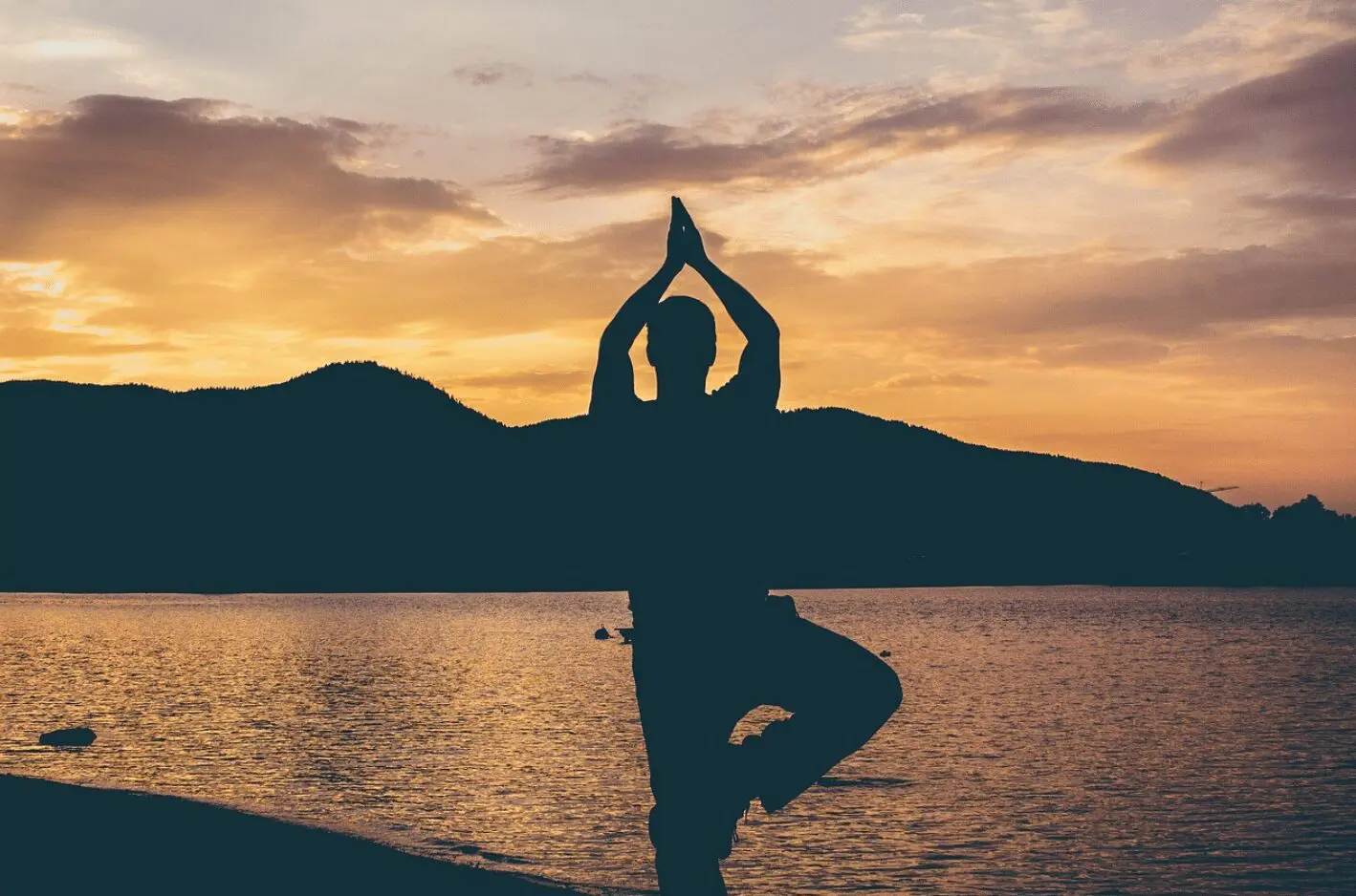 Silhouette of a man doing yoga on the beach at sunset during wedding planning.