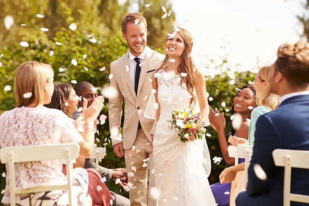 A bride and groom, surrounded by confetti, elegantly walking down the aisle on their special day.