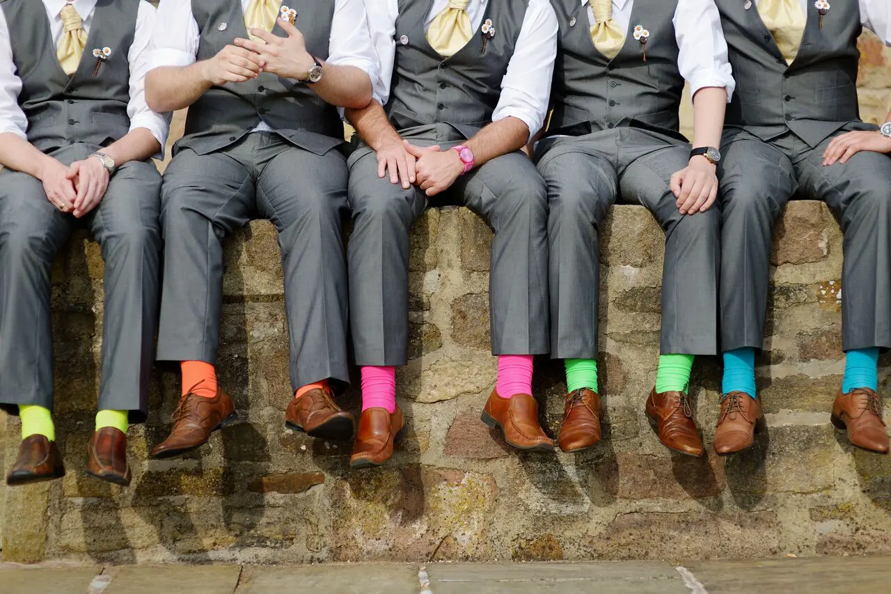 A group of groomsmen sitting on a stone wall during a wedding ceremony in the UK.