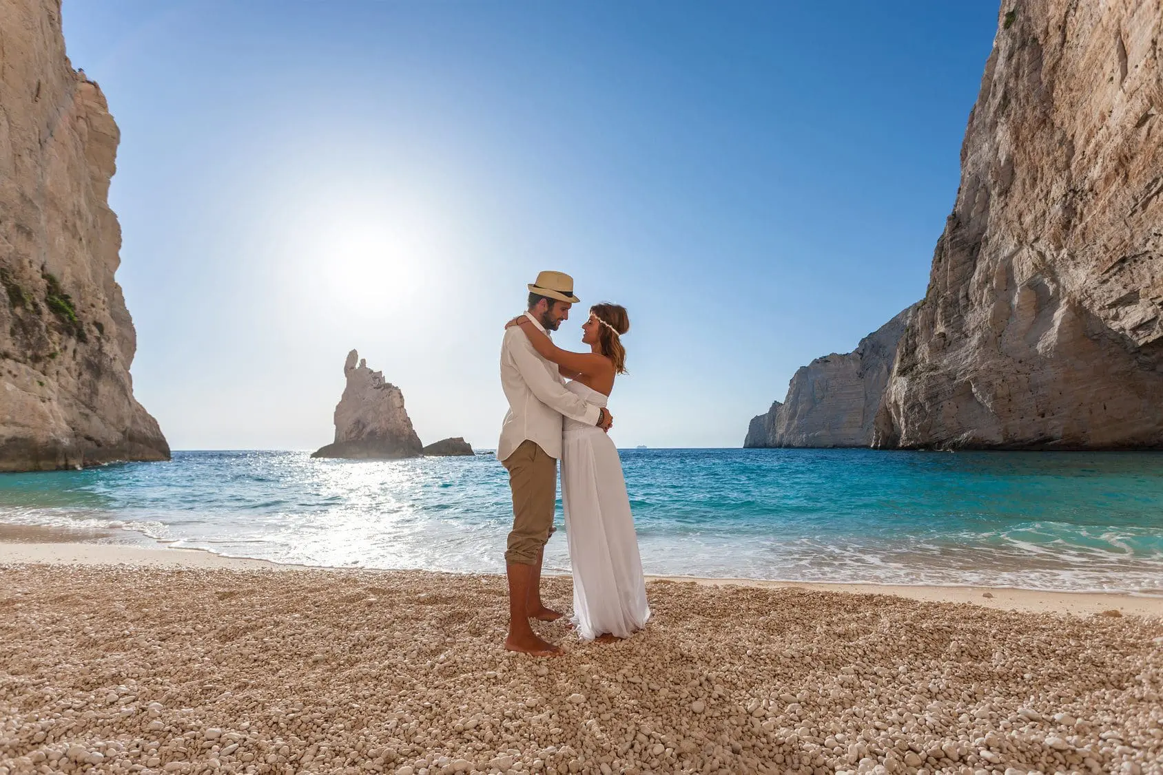A couple is embracing on a beach in Greece, capturing their romantic wedding ceremony.