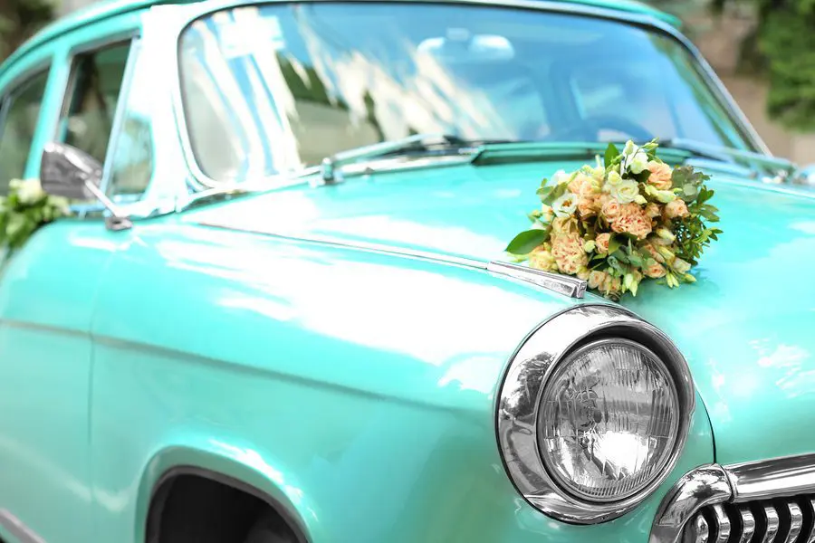 A vintage car adorned with flowers on the hood, perfect for wedding services or planning in the UK.