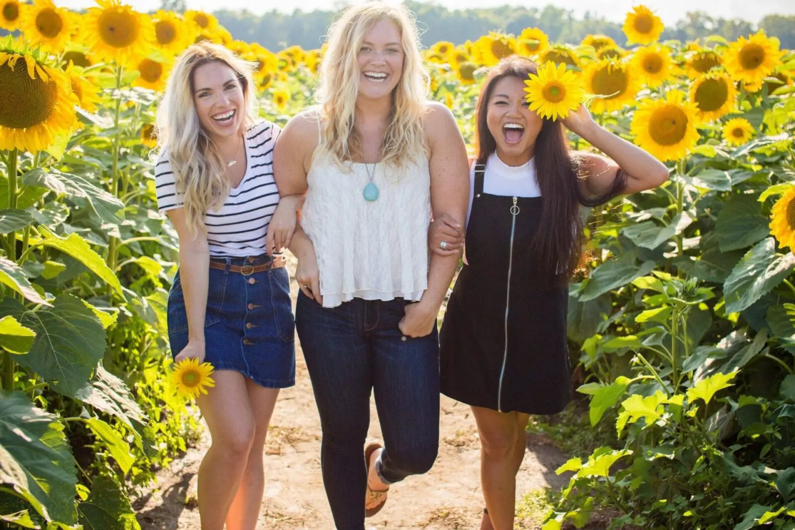 Three women standing in a field of sunflowers.