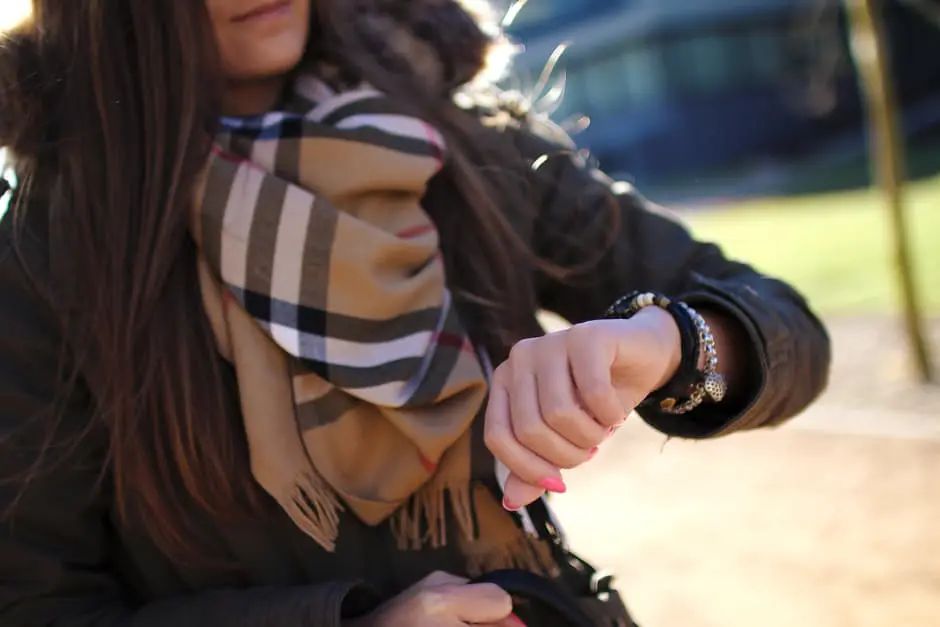 A woman wearing a scarf and a watch, meticulously planning her wedding.