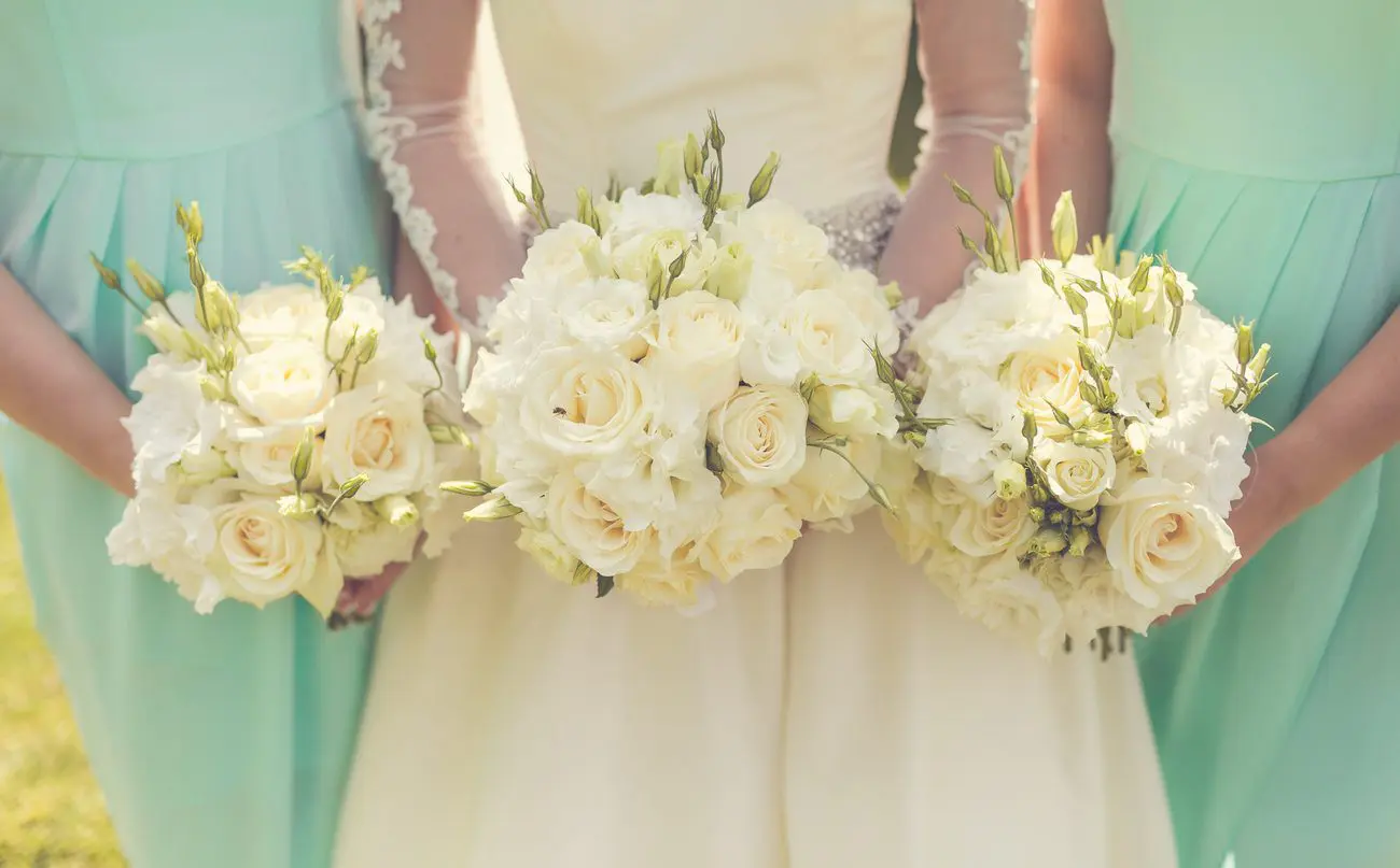 Three bridesmaids holding bouquets of white roses at a wedding in the UK.