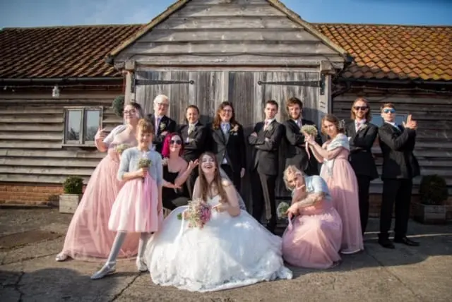 A wedding party posing in front of a barn.