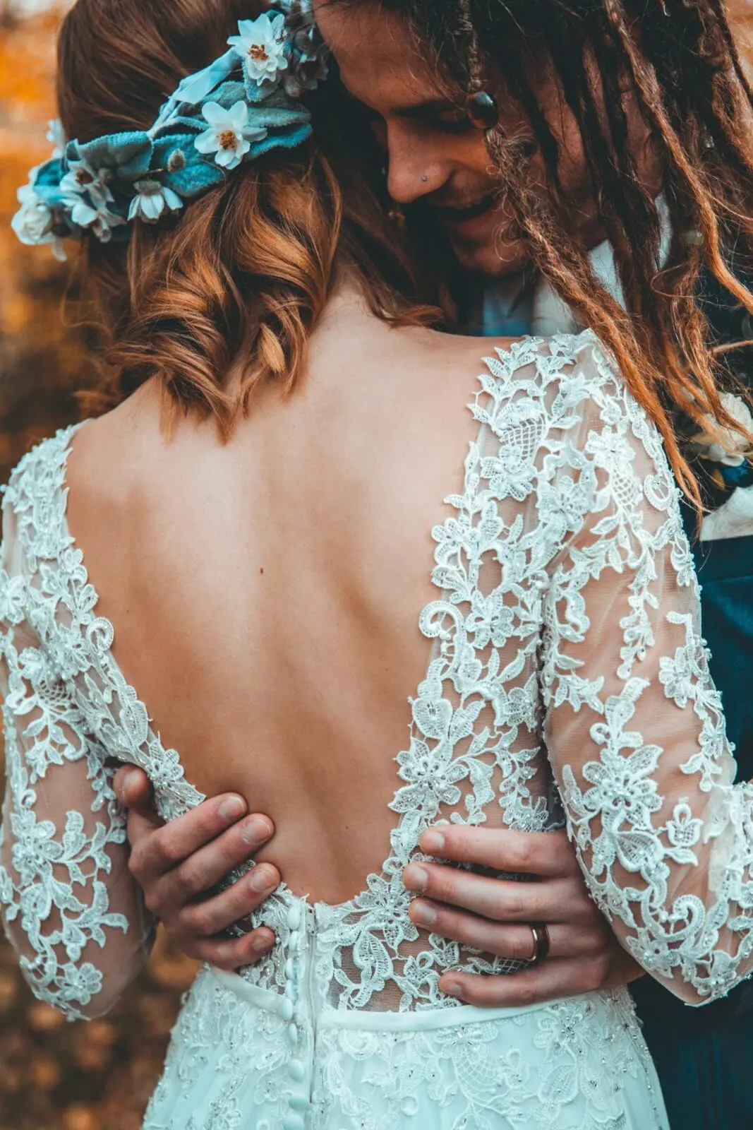 A bride and groom with dreadlocks hugging in the woods during their wedding.