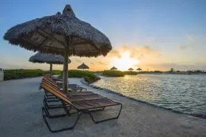 A beach with lounge chairs and thatched umbrellas at sunset, perfect for wedding ceremonies and receptions.