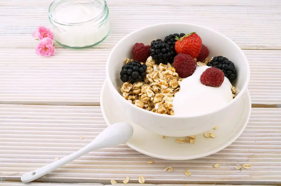 A bowl of granola and yogurt topped with fresh berries on a wooden table.