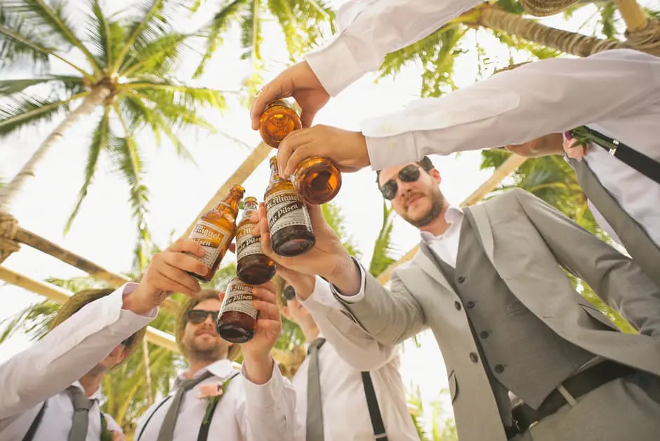A group of groomsmen raising a bottle of beer during wedding celebrations.