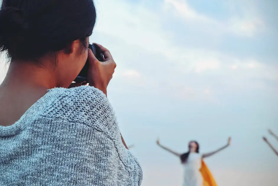 A woman captures a picture of a group of people on the beach while providing wedding services.