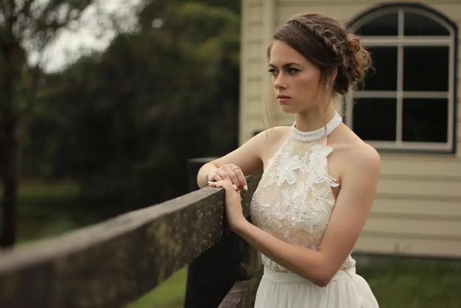 A woman in a white dress preparing for her wedding, leaning against a fence.