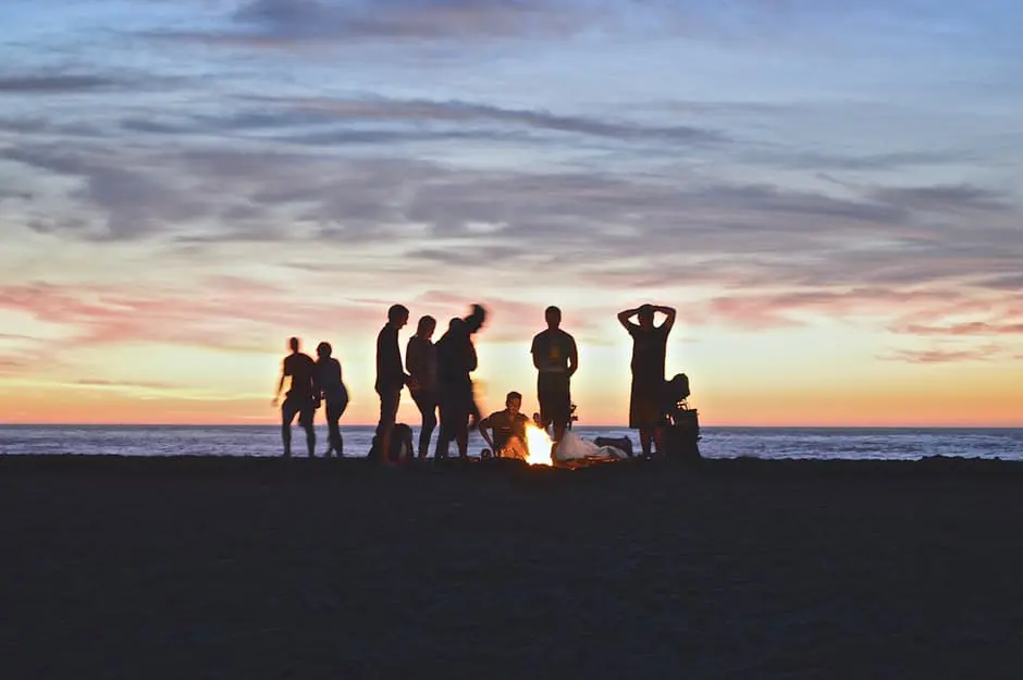 A group of people standing around a campfire on the beach during a wedding uk