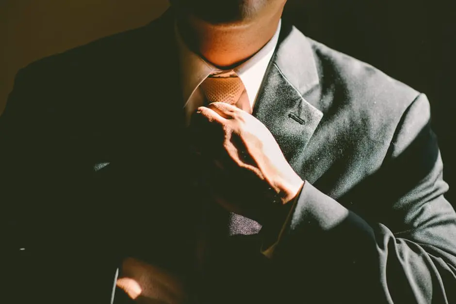 A man in a suit adjusts his tie for a wedding.