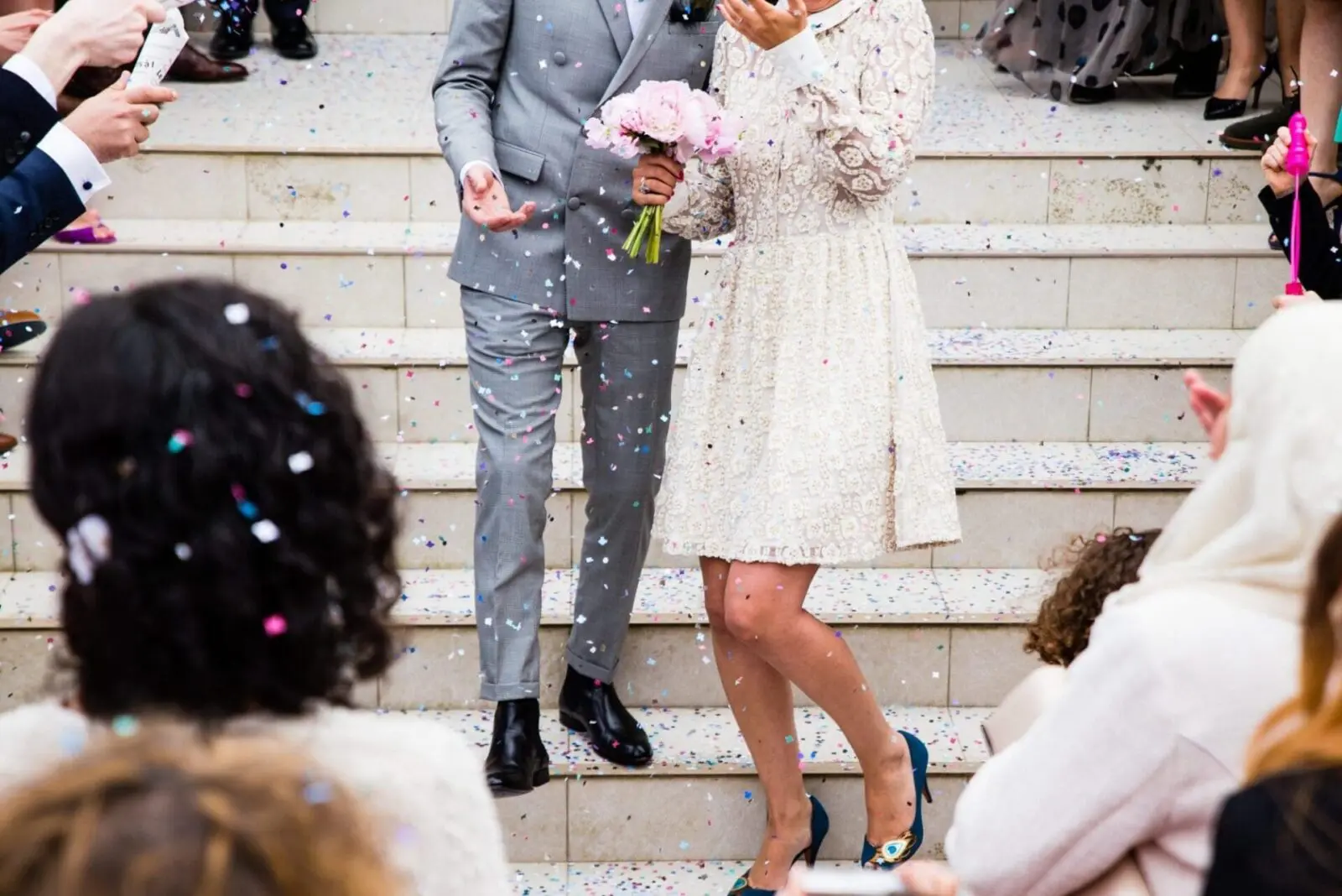 A bride and groom, amidst their wedding planning, stand on elegant steps while joyous confetti is jubilantly thrown at them.