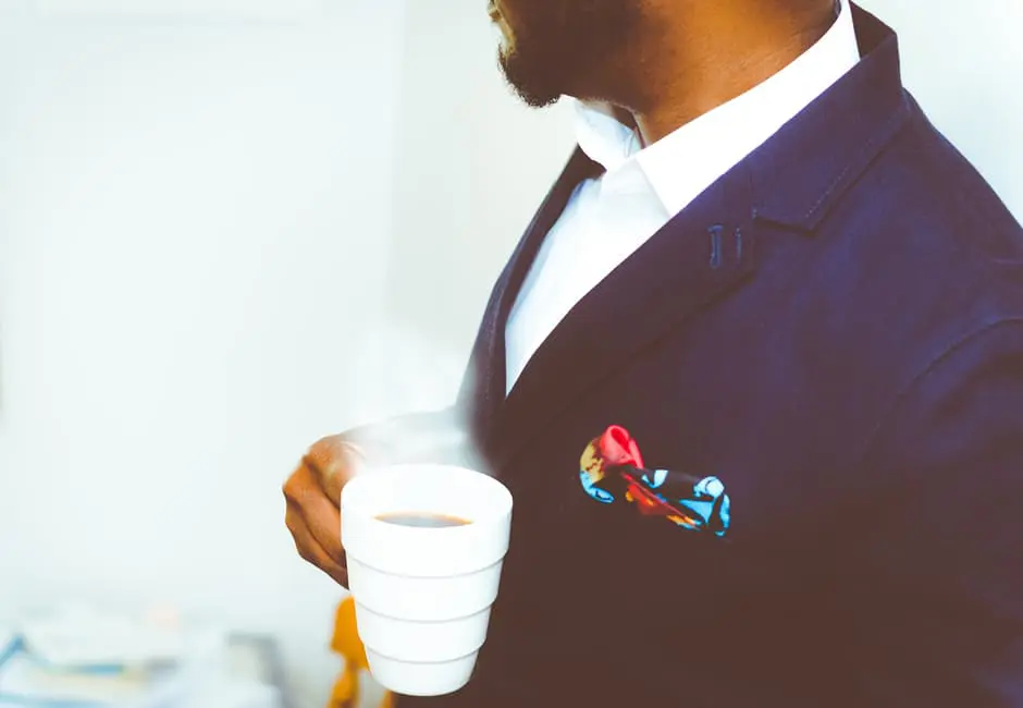 A man in a suit is holding a cup of coffee while planning for a wedding in the UK.