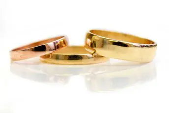 Three gold wedding rings on a white surface for wedding planning.
