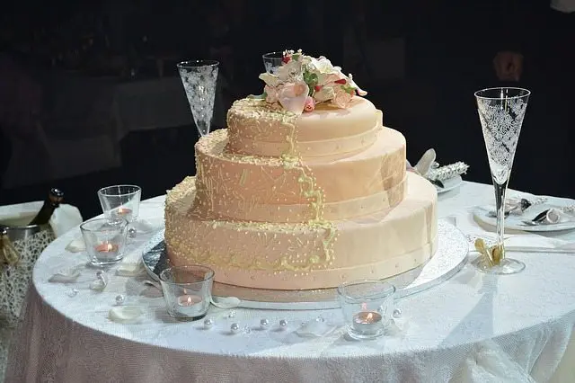 A three tier wedding cake sits on a table at a wedding in the UK.
