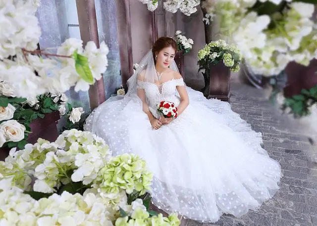 A bride in a white wedding dress posing in front of flowers for her perfect wedding in the UK.