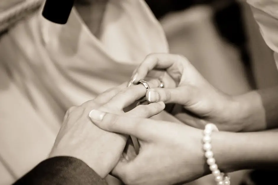 A woman is performing a wedding ceremony and putting a wedding ring on someone's finger.