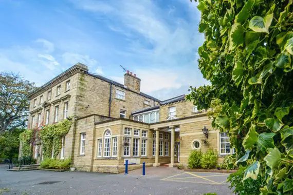 A large, historic stone building with multiple stories is surrounded by lush greenery under a bright blue sky, making it an ideal location for wedding planning or hosting unforgettable wedding services.