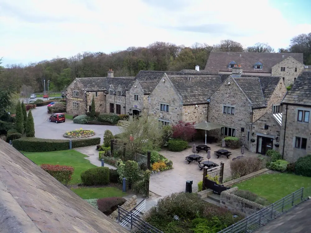 A view of a small stone-built village with neatly landscaped gardens, outdoor seating, and a red car parked on a driveway—an idyllic setting perfect for planning wedding services.