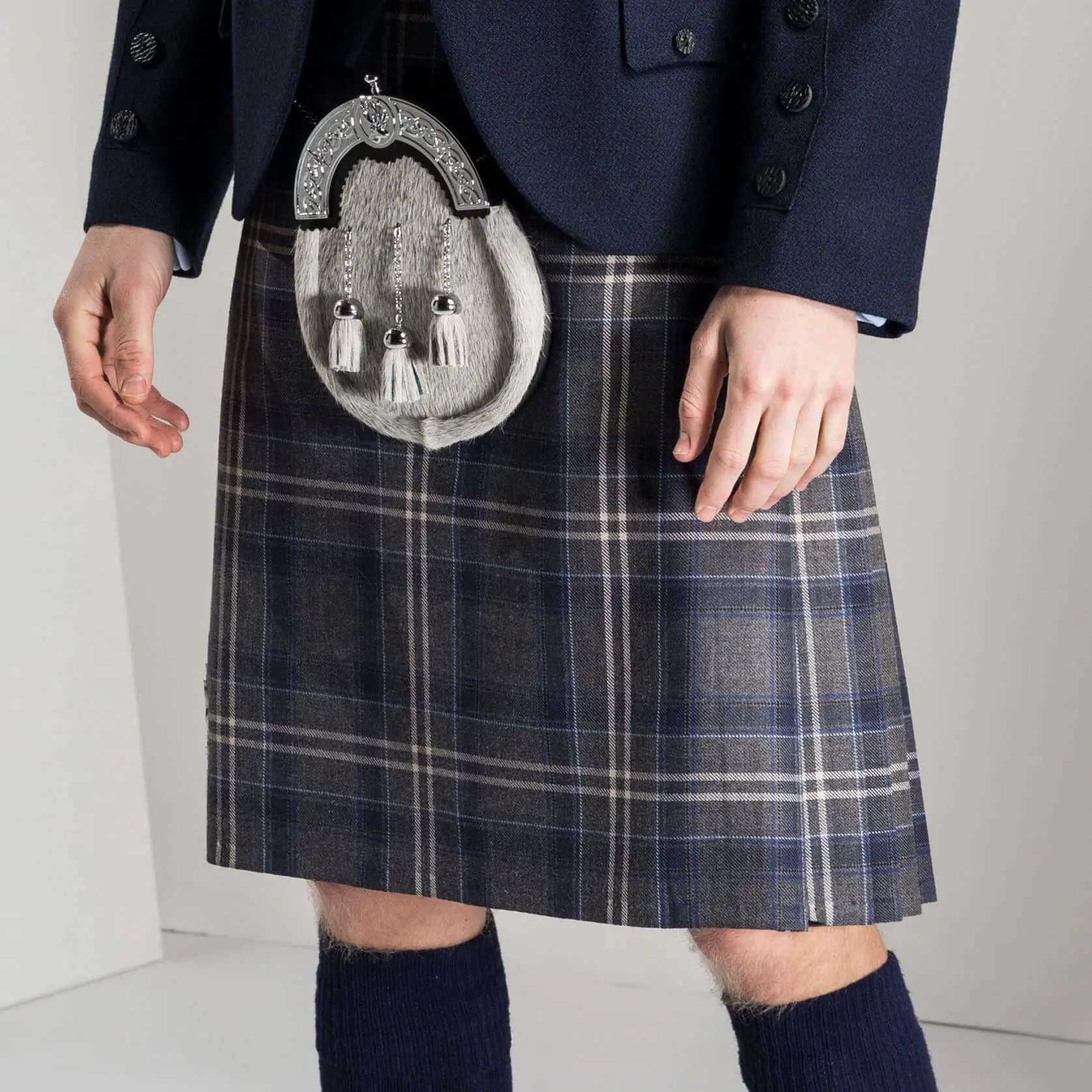 A person wearing a tartan kilt with a sporran, a dark jacket, and knee-high socks.