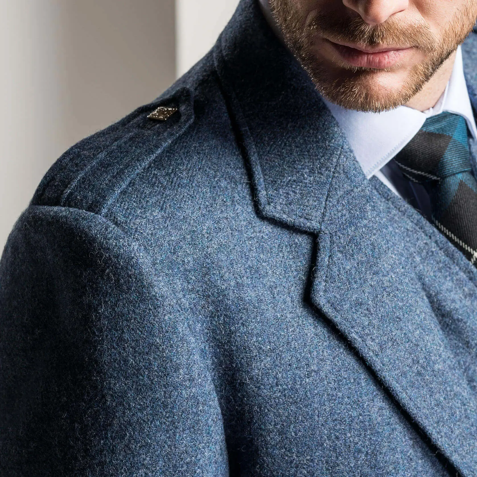 Close-up of a person wearing a blue coat with a tie and white shirt. The focus is on the upper part of the coat, showcasing its texture and details.