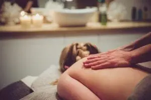 Individual receiving a back massage in a spa setting, with lit candles on a counter in the background.