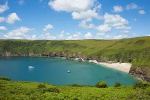 A scenic coastal bay with clear blue water, sandy beach, green cliffs, and a few anchored boats on a sunny day with scattered clouds—an idyllic setting perfect for any wedding planning business.