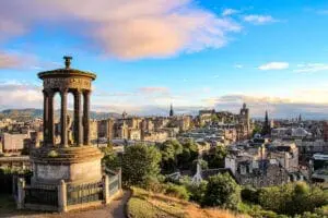 View of Edinburgh from Calton Hill, showing the Dugald Stewart Monument in the foreground and a panorama of the cityscape with historic buildings under a blue sky with scattered clouds – an idyllic backdrop perfect for wedding services.