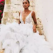 A woman in a white, ruffled wedding gown poses in front of a textured stone wall.