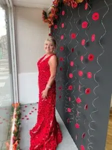 Woman in a long red dress adorned with poppies stands against a black backdrop covered in red poppy decorations.