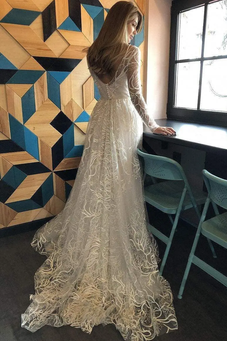 A woman in a long, white, intricately designed dress faces away, standing by a table with teal chairs, next to a window and a geometric patterned wall.
