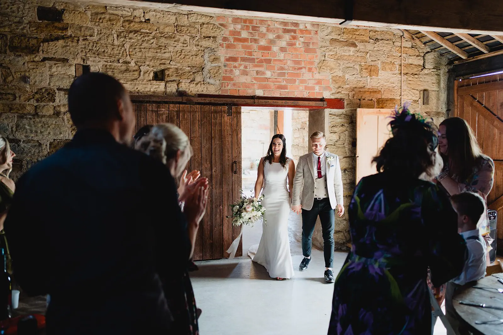 A couple walks down the aisle at an indoor wedding venue, surrounded by applauding guests, experiencing the seamless magic crafted by a top-tier wedding business.