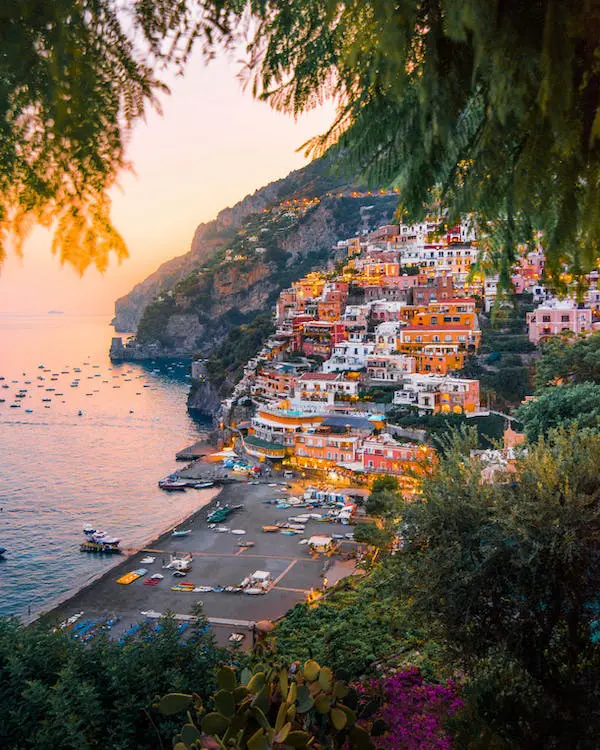 A coastal town with colorful buildings on a hillside overlooks a bay dotted with boats at sunset, creating the perfect romantic backdrop for wedding planning.