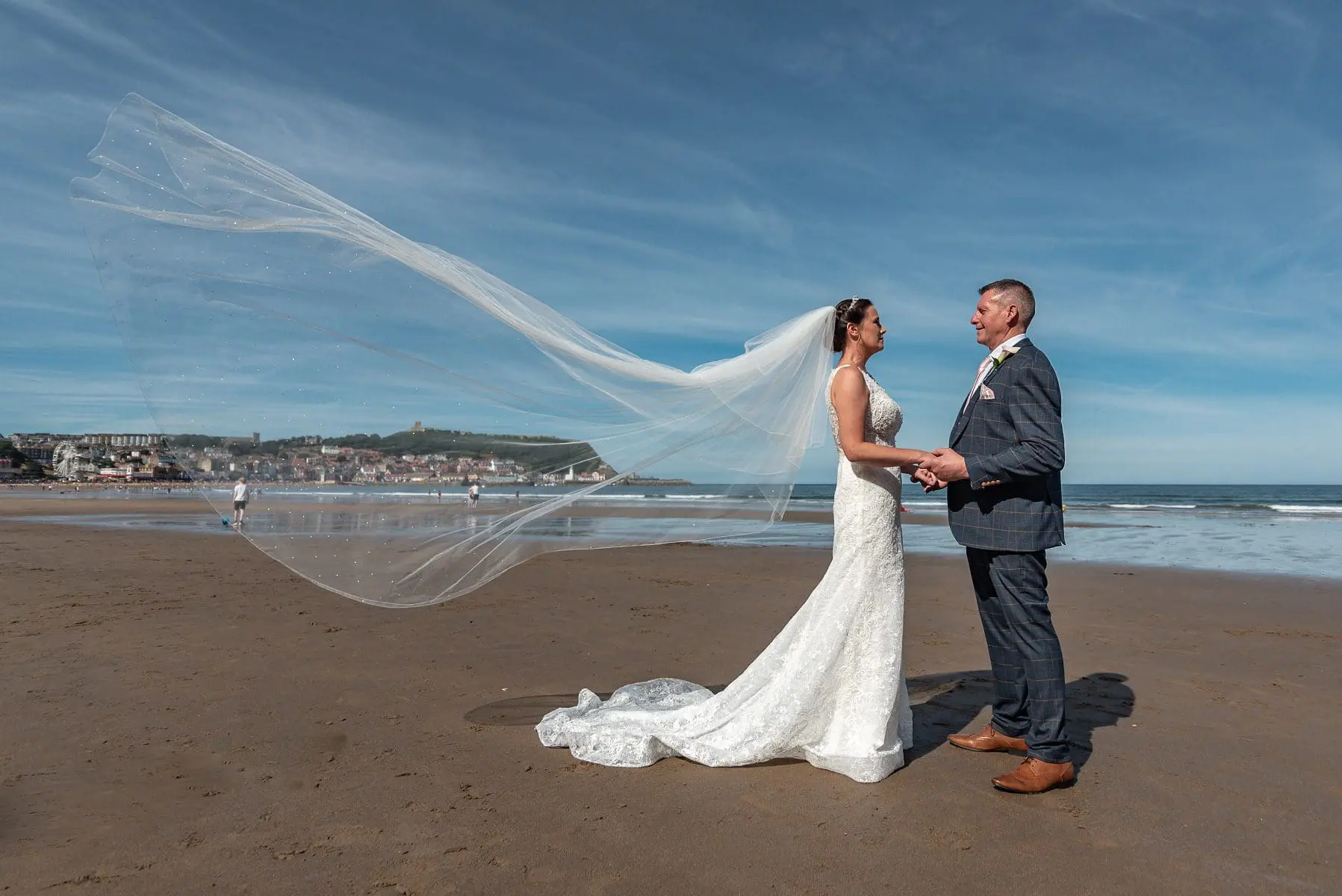 Bride and groom holding hands on a beach, with the bride's veil flowing in the wind—a perfect moment captured by exceptional wedding planning.