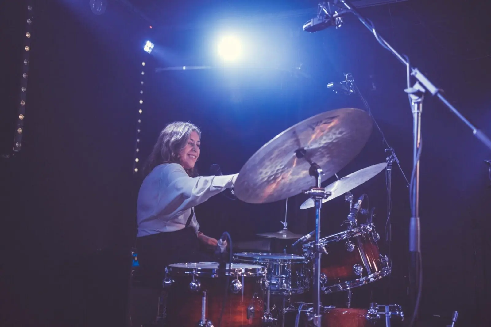 A person is playing drums on a dimly lit stage with spotlights above, setting a rhythmic tone that could seamlessly fit into wedding services.