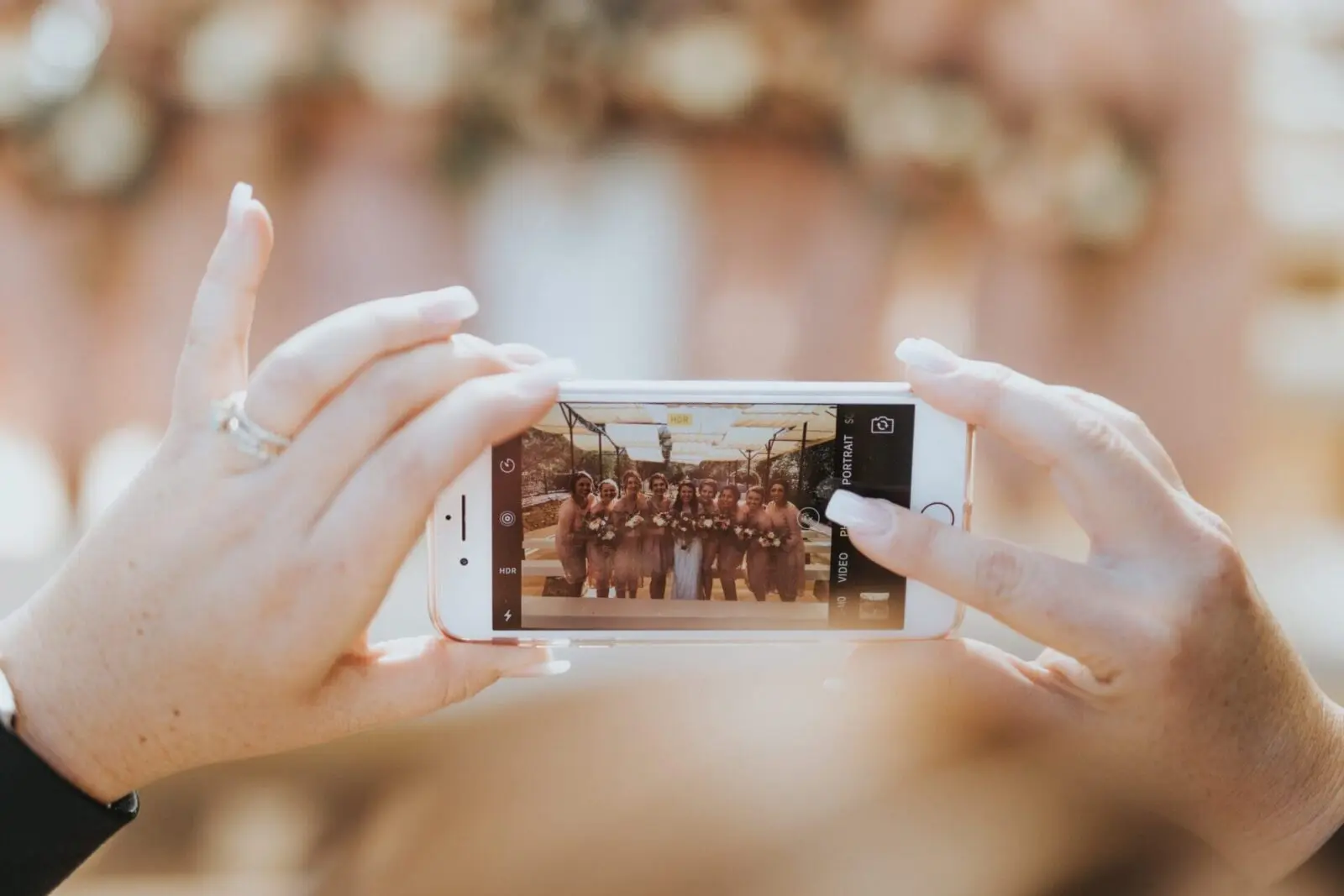 A person holds a smartphone, capturing a cherished moment at a wedding, where the bridesmaid dresses add a splash of elegance to the scene.