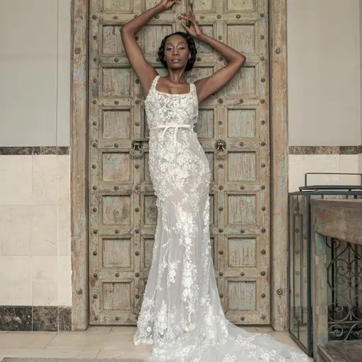 A person in a lace gown poses gracefully in front of a decorative wooden door, capturing the essence of refined elegance often seen in bespoke wedding planning.