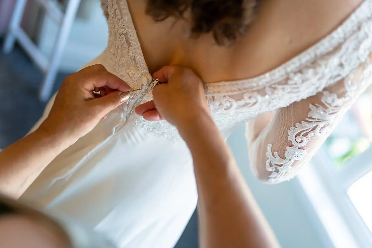 Person fastening the buttons on the back of a white lace wedding dress.